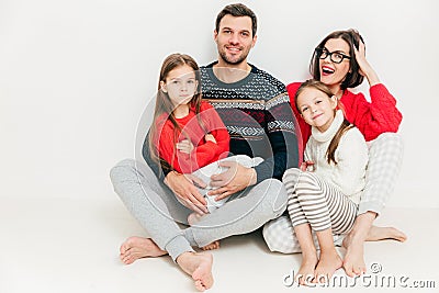 Portrait of happy family of four members: attractive brunette woman, her husband and two small daughters sit on floor, isolated o Stock Photo