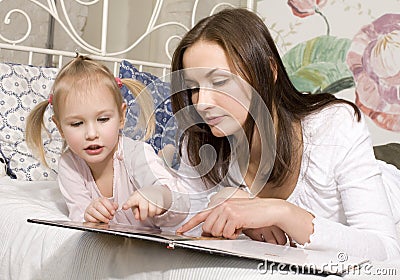 Portrait of happy family, mother and daughter in bed reading book Stock Photo