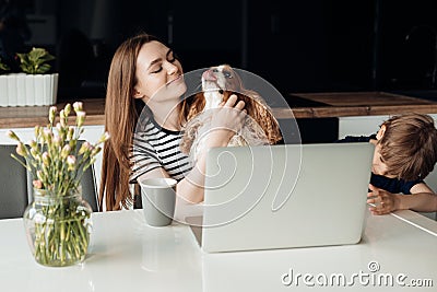 Portrait of happy family. Young woman sitting at table with little boy son, holding stroking spaniel, working on laptop. Stock Photo