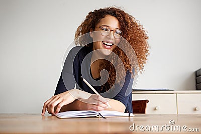 Happy female college student sitting at desk writing in book Stock Photo