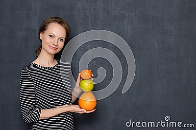 Portrait of happy girl smiling and holding colorful stack of fruits Stock Photo