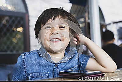 Portrait happy kid looking out with smiling face, Little boy watching cartoo or play games on mobile phone while waiting for food Stock Photo