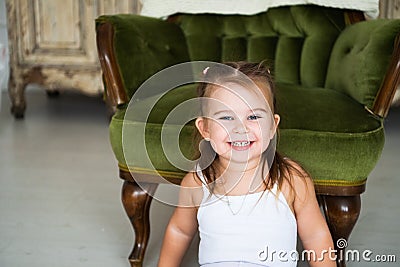 Portrait of a happy laughing child girl sitting on the floor near the antique chair Stock Photo
