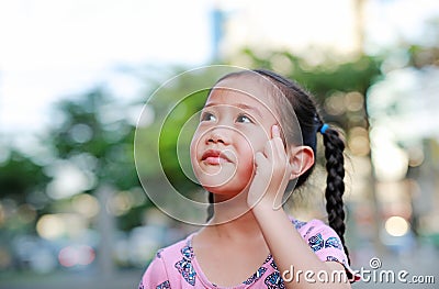 Portrait of happy little Asian child in garden with thinking and looking up. Close-up smiling kid girl with forefinger point on Stock Photo