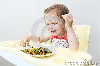 Portrait of happy little 2 years girl eating fish with vegetable Stock Photo