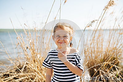 Portrait of a happy lively little girl by the lake at spring, dry grass around Stock Photo