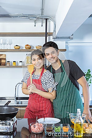 Portrait of happy lovely young Asian couple in love with casual clothes in modern kitchen, is smiling, looking at camera and Stock Photo
