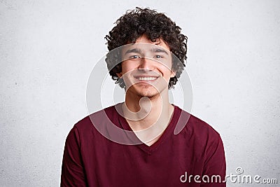 Portrait of happy male with broad smile, has curly hair, pleasant smile, dressed casually, stands against white background. Deligh Stock Photo