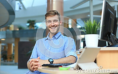 Portrait of happy man sitting at office desk, looking at camera, smiling. Stock Photo