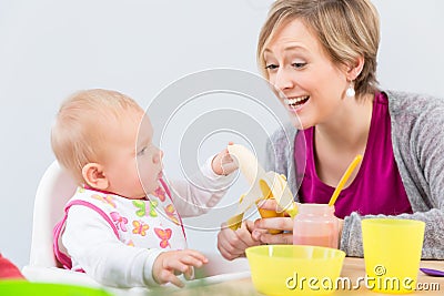 Happy mother giving a fresh and nutritious banana to her cute baby girl Stock Photo