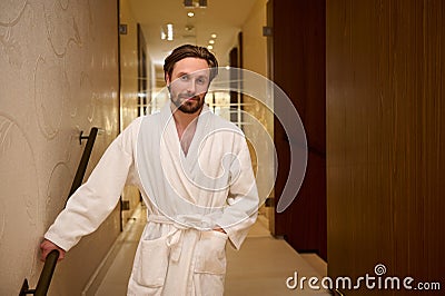 Portrait of a happy relaxed handsome middle aged European man dressed in white terry bathrobe standing on the hallway of a luxury Stock Photo