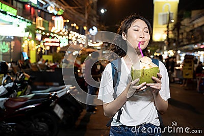 Portrait of happy relaxing Asian solo hipster traveller holding a coconut drink on street in Bangkok, Thailand. Female Stock Photo