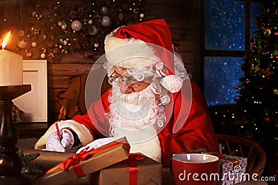 Portrait of happy Santa Claus sitting at his room at home near Christmas tree and answering Christmas letters Stock Photo