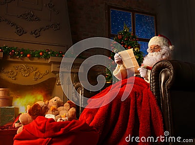 Portrait of happy Santa Claus sitting at his room at home near Christmas tree and reading Christmas letter or wish list. Stock Photo