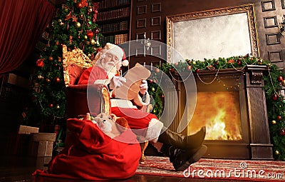 Portrait of happy Santa Claus sitting at his room at home near Christmas tree and reading Christmas letter or wish list. Stock Photo