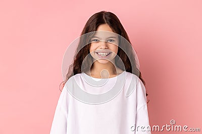 Satisfied little girl in T-shirt looking at camera with toothy smile, expressing positive expression Stock Photo