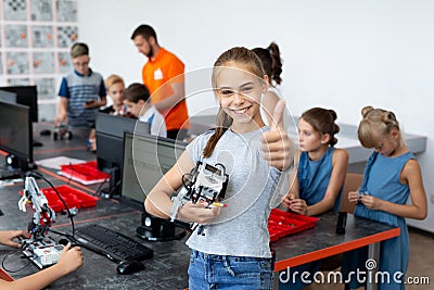 Portrait of a happy schoolgirl girl in a robotics class, she holds a robot assembled from plastic parts programmed on a Stock Photo