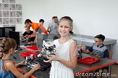 Portrait of a happy schoolgirl girl in a robotics class, she holds a robot assembled from plastic parts programmed on a Stock Photo