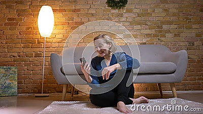 Portrait of happy senior caucasian lady sitting on floor and talking in videochat using smartphone in cozy home Stock Photo