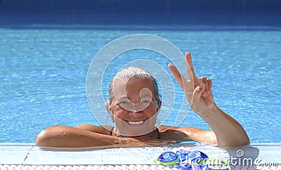 Portrait of an happy senior sporty woman enjoying swimm into the swimming pool doing ok gesture with hand - active retiree Stock Photo