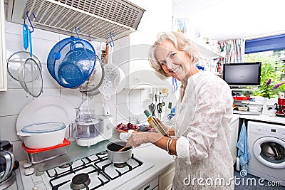 Portrait of happy senior woman preparing food in domestic kitchen Stock Photo