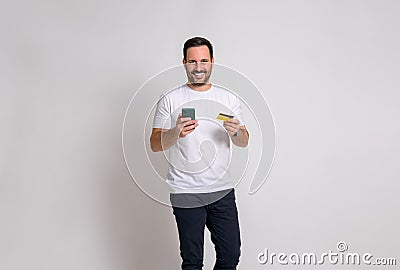Portrait of happy shopaholic man with credit card making mobile payment against white background Stock Photo