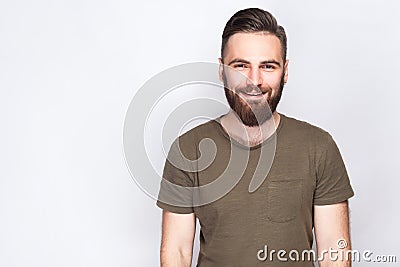 Portrait of happy smiley bearded man with dark green t shirt against light gray background. Stock Photo