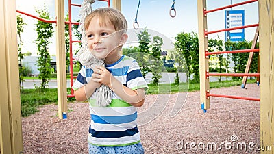 Portrait of happy smiling toddler boy playing with big rope for climbing on the children palyground at park. Active and Stock Photo