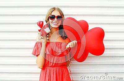 Portrait happy smiling woman holding in hands gift box and red air balloons heart shape over white Stock Photo