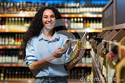 Portrait of happy and smiling woman shopper in supermarket, latin american woman choosing alcohol wine using app on Stock Photo