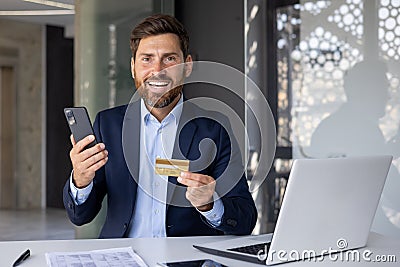 Portrait of a happy and smiling young businessman, banker sitting in a suit in the office at the table with a laptop Stock Photo
