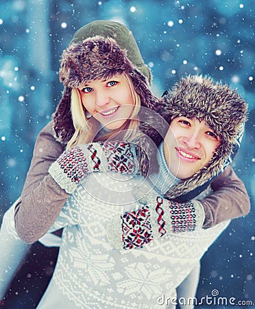 Portrait happy smiling young couple in winter day having fun, man giving piggyback ride to woman over snowflakes Stock Photo
