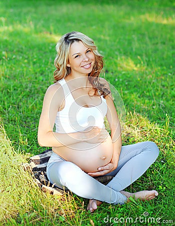 Portrait happy smiling young pregnant woman sitting on grass doing yoga Stock Photo