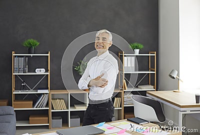 Happy confident successful senior businessman standing by office desk and smiling Stock Photo