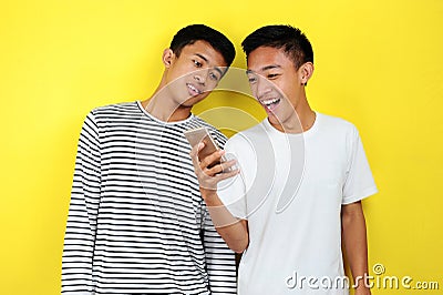 Portrait of happy two casual men smiling look at smartphone. Portrait of handsome two young men looking at their phone and smiling Stock Photo