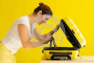 Portrait of a happy woman packs a mini bikini in a suitcase on a yellow background. The girl is going on a trip to the Stock Photo