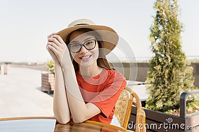 Portrait of a happy woman sitting in a summer cafe waiting for an order on a beautiful promenade. Stock Photo