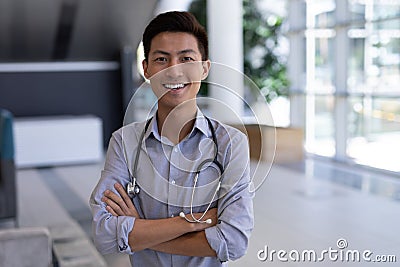 Happy Asian male doctor standing with arms crossed in hospital Stock Photo