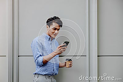 Portrait of a Happy Young Businessman Using Mobile Phone. Lifestyle of Modern People. Standing by the Wall Stock Photo