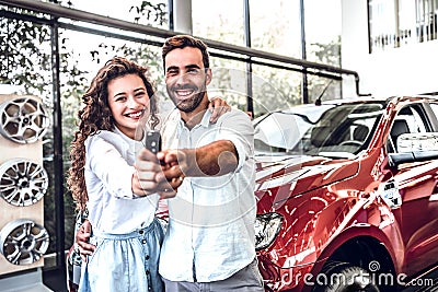 Portrait of a happy young couple hugging in a car salon showing car keys to a newly bought vehicle Stock Photo