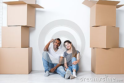 Portrait of happy young couple sitting on floor looking at camera and dreaming their new home and furnishing. Stock Photo