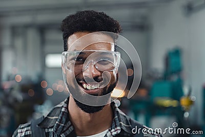 Portrait of happy young industrial man working indoors in metal workshop, looking at camera. Stock Photo