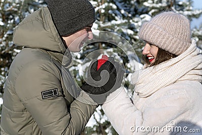 Portrait of happy young loving couple in winter forest. Guy warms his girlfriends hands Stock Photo