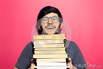 Portrait of happy young man holding bunch of books, wearing round eyeglasses on background of coral pink. Stock Photo