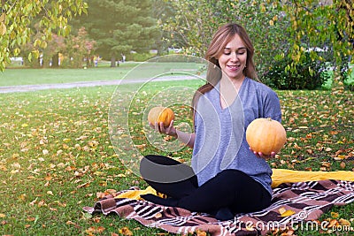 Portrait of happy young pregnant model sitting with crossed legs on grass lawn and looking at her belly with gentle smile. Future Stock Photo