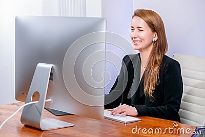 Portrait of happy young successful businesswoman at office. She sits at the table, looks at the display and laugh, office work. Bl Stock Photo