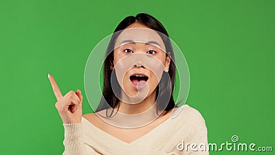 Portrait of happy young woman in asian pointing finger up isolated over green background Stock Photo