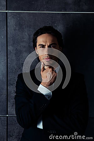 Portrait of harsh young man in formalwear thinking and holding his chin Stock Photo