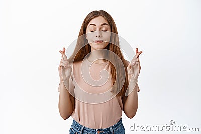 Portrait of hopeful girl student wishing about exam, cross fingers for good luck and close eyes, praying, pleading for Stock Photo