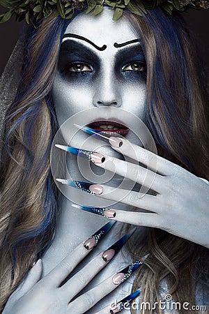 Portrait of a horrible scary Corpse Bride in wreath with dead flowers, halloween makeup and long manicure.Design of Stock Photo